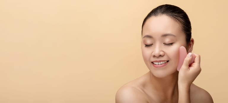 A serene Asian woman with closed eyes gently presses a pink gua sha stone