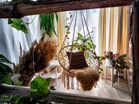 A modern cozy beautiful room with a braided rope macrame chair, green plants and a window with curtains. Interior and background. Location for photo shooting