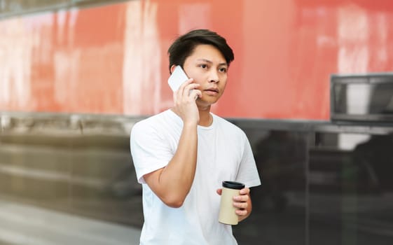 Concentrated asian guy talking on phone, drinking coffee
