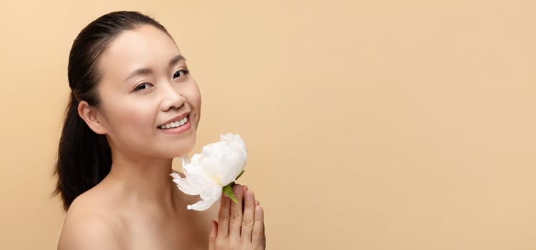 Cheerful millennial chinese naked woman with white flower, enjoy treatment