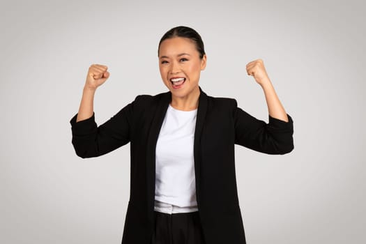Exuberant Asian businesswoman in a smart black suit with fists pumped in the air