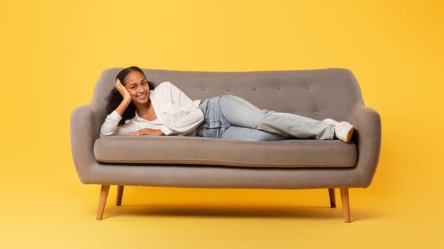 Carefree African American teenage girl relaxing lying on sofa, studio