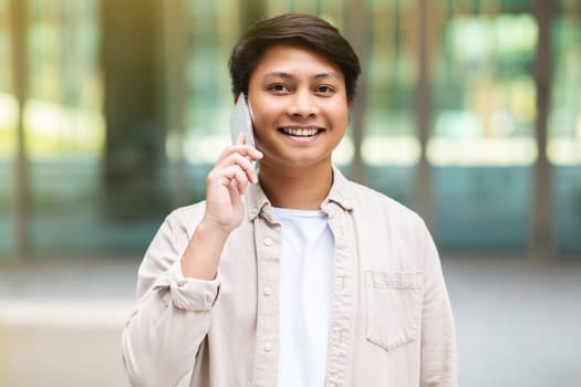 Young asian guy talking on phone while walking by city