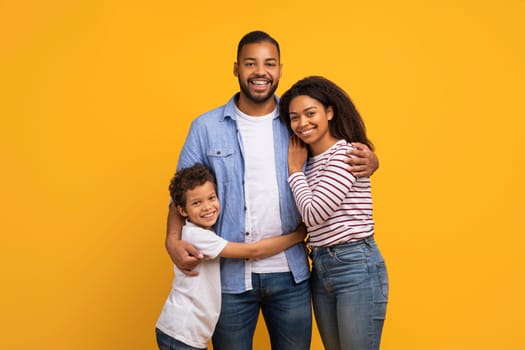 Cheerful black family of three with little son sharing loving embrace