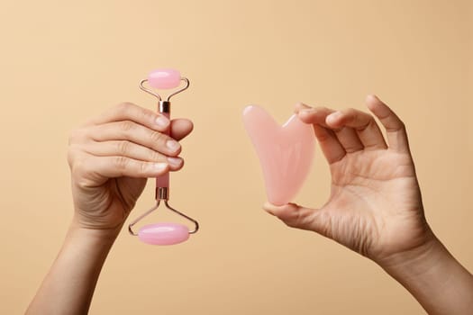 Two hands elegantly display a pink facial roller and a rose quartz gua sha tool