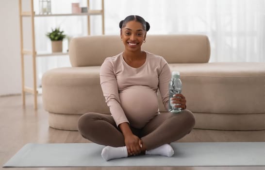 Happy african american pregnant woman drinking water after workout