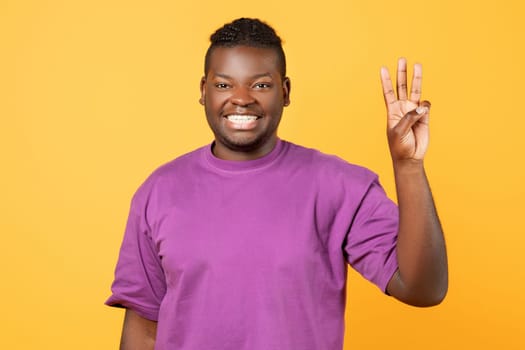 Cheerful African American guy raising hand showing three fingers, studio