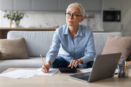 senior woman sitting with laptop and taking notes at home