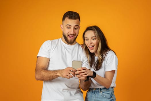 Glad surprised young european man and woman look at smartphone, watch video