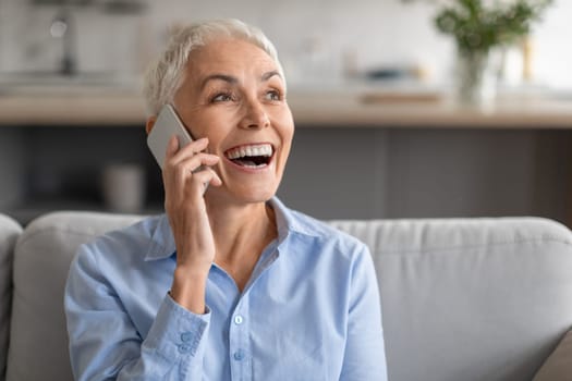 Happy attractive mature businesswoman laughing talking by smartphone at home