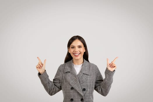 Cheerful woman in plaid jacket pointing upwards with both hands