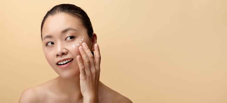 Happy millennial chinese naked lady put cream on face, enjoy procedure