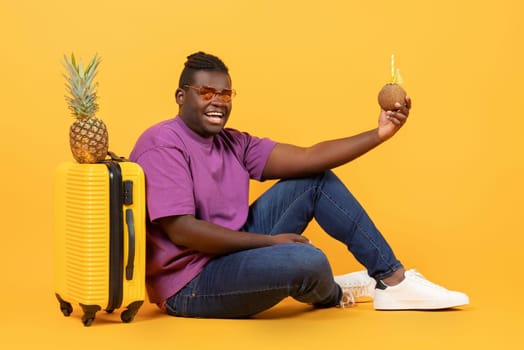 black guy near suitcase holding pineapple and coconut drink, studio