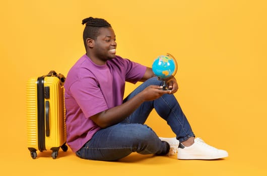 African American Traveler Man Holds Globe Sitting Near Suitcase, Studio