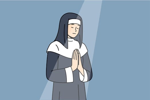 Nun prays to god with palms folded in front chest, standing under beam light in cathedral building