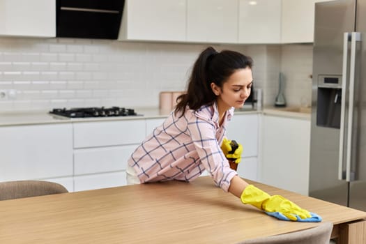 young woman cleaning wooden table with microfiber cloth.