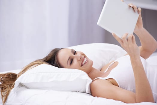 Happy woman, bed and relax with tablet for social media, communication or networking at home. Female person smile lying in bedroom on pillow with technology for online streaming or entertainment.