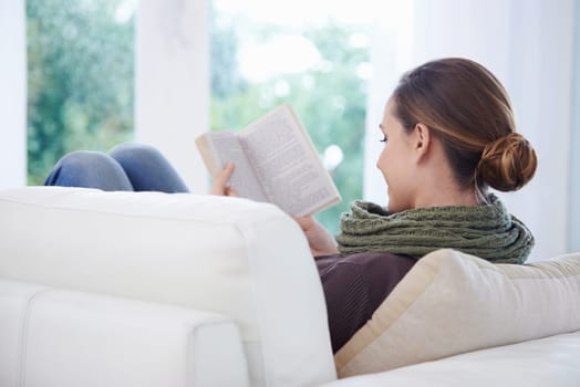 Woman, book and reading in home from the back for story, novel and learning knowledge on sofa in living room. Lady, fiction books and relax on couch with literature, hobby and comfortable in lounge