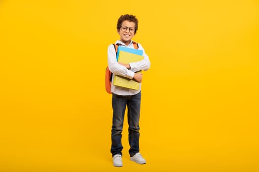 Schoolboy with glasses and school supplies on yellow background