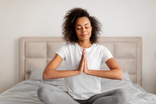 Calm black young woman meditating in lotus position at bedroom