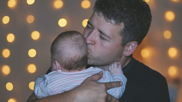 A father kisses his child in his arms at the evening lights.