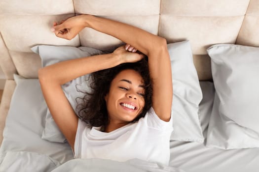 Well rested african american woman leisurely wakes up stretching arms