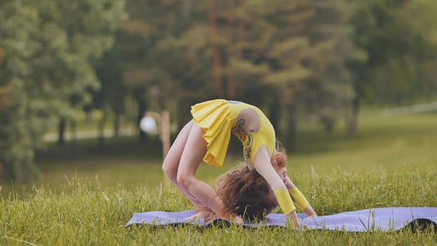 A little girl performs the elements of rhythmic gymnastics in the park.