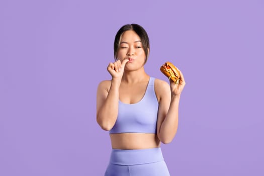 Asian woman in fitness gear hesitantly trying fast food burger