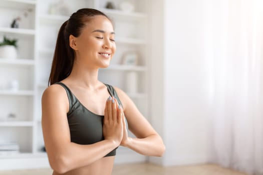 Beautiful asian woman practicing yoga with eyes closed and making namaste gesture
