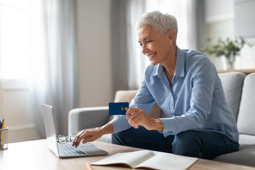 senior lady with credit card websurfing laptop for purchases indoors