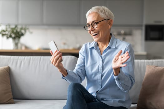 Excited mature woman in eyewear reading news on cellphone indoor
