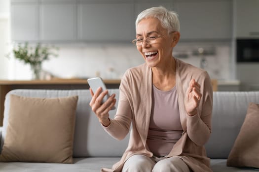 Cheerful senior woman using smartphone and having fun at home