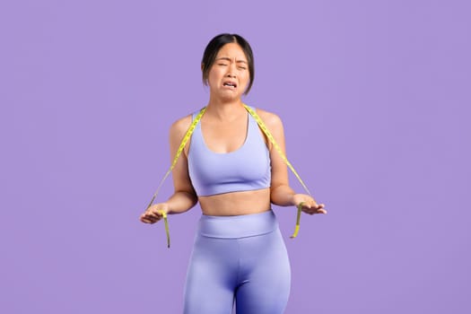 Asian woman in sportswear with measuring tape crying