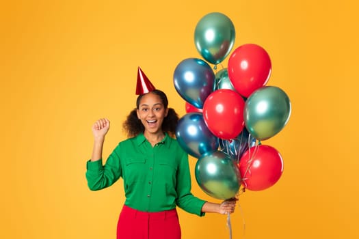 African teenager girl posing with balloons gesturing yes, yellow background
