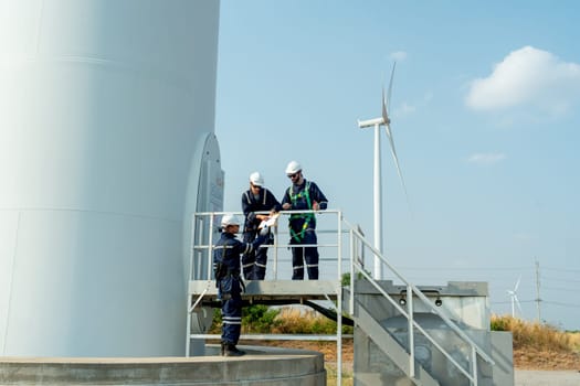 Wide shot of one professional technican worker give the document to his coworker stand in base of windmill or wind turbine.