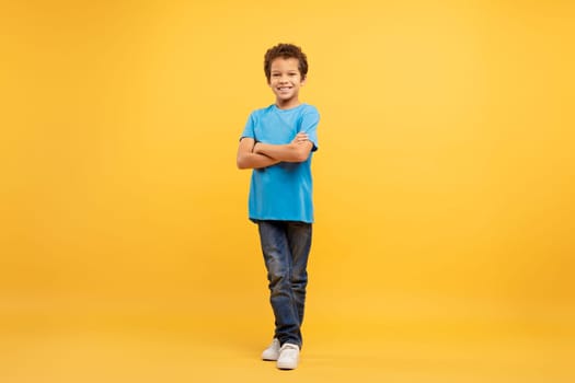 Confident latin boy with arms crossed in blue shirt, yellow background