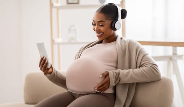 Happy pregnant black woman listening to music