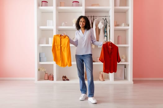 Happy woman with two colorful shirts in closet