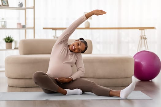 Cheerful pregnant young black woman exercising at home