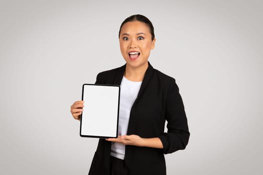 Excited Asian businesswoman presenting a tablet with a blank screen, perfect for mockups