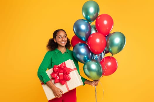 black girl holds gift box and bunch of balloons, studio