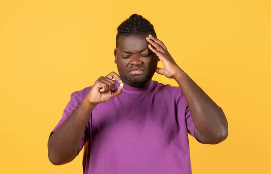 Black young man suffering from headache holding medical pill, studio