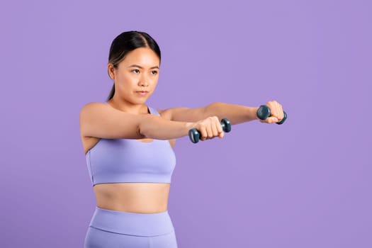 Determined asian woman exercising with dumbbells