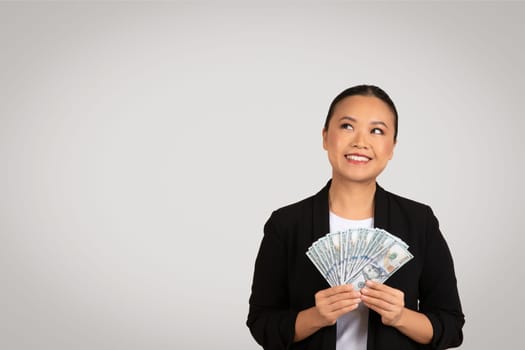 Optimistic Asian businesswoman holding and displaying a fan of US dollar bills