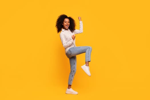 Joyful african american woman dancing on yellow background