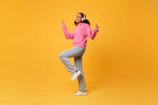 black girl in headphones listens music dancing over yellow background