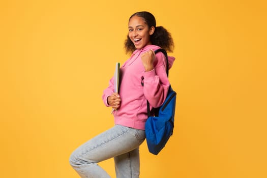 Happy black teen student lady gesturing yes on yellow background