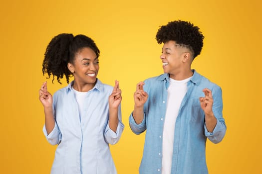 Optimistic young African American siblings in light blue attire make wishing gestures