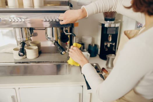 Close up of female barista cleaning coffee machine at coffee shop after froths milk