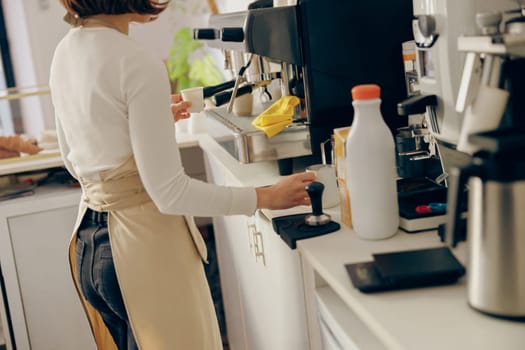 Close up of female barista frothing milk for coffee with professional coffeemaker working in cafe